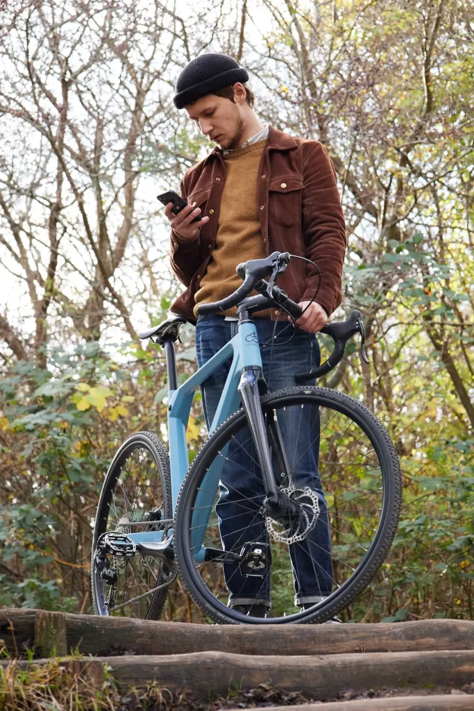 Young man checking his phone in the woods while holding a Mattis gravel bike