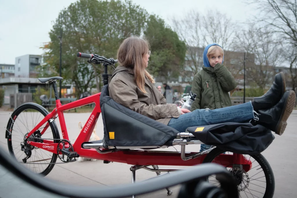 Mother relaxing in the front bed of VeloSled Anna cargobike while talking to her child